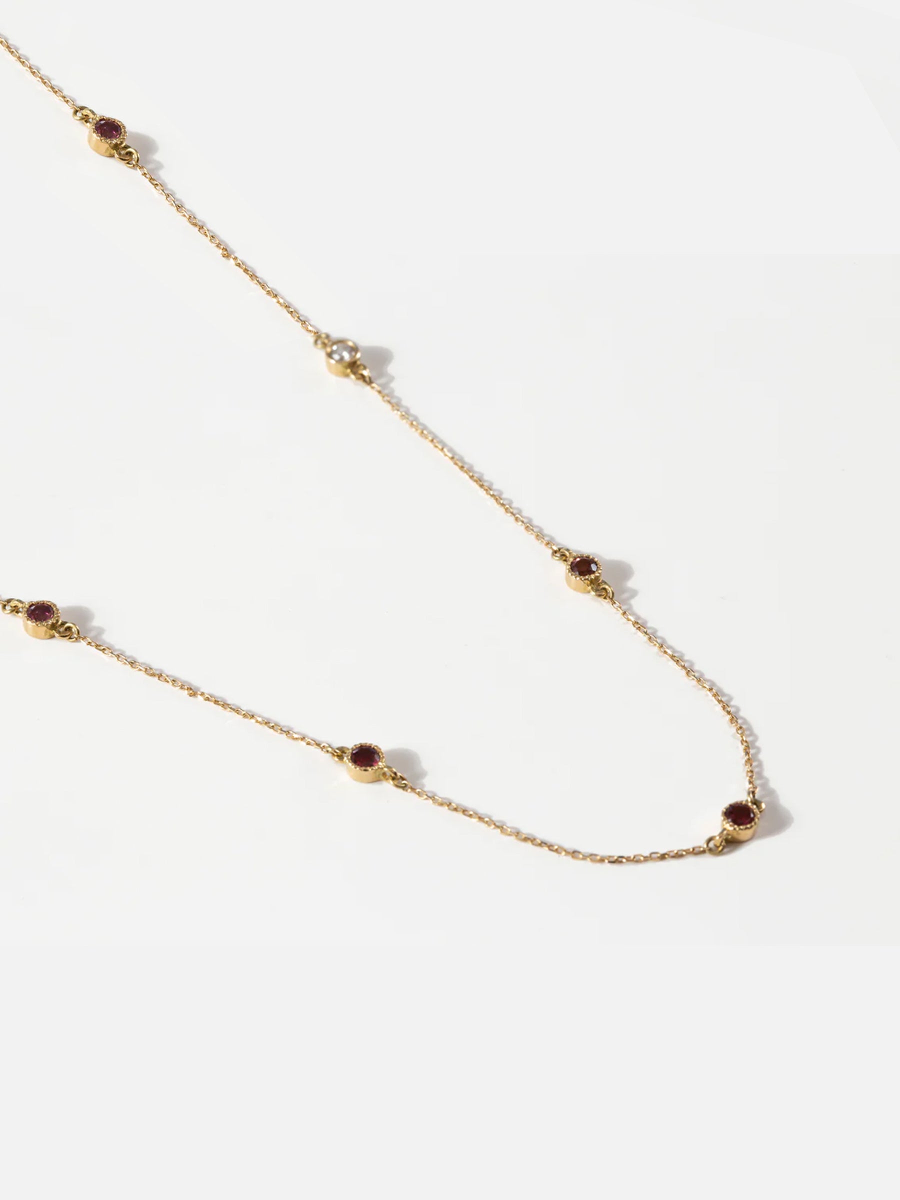 Side-angle view of the 18k gold long necklace with round pink tourmaline stones and a brilliant diamond accent.