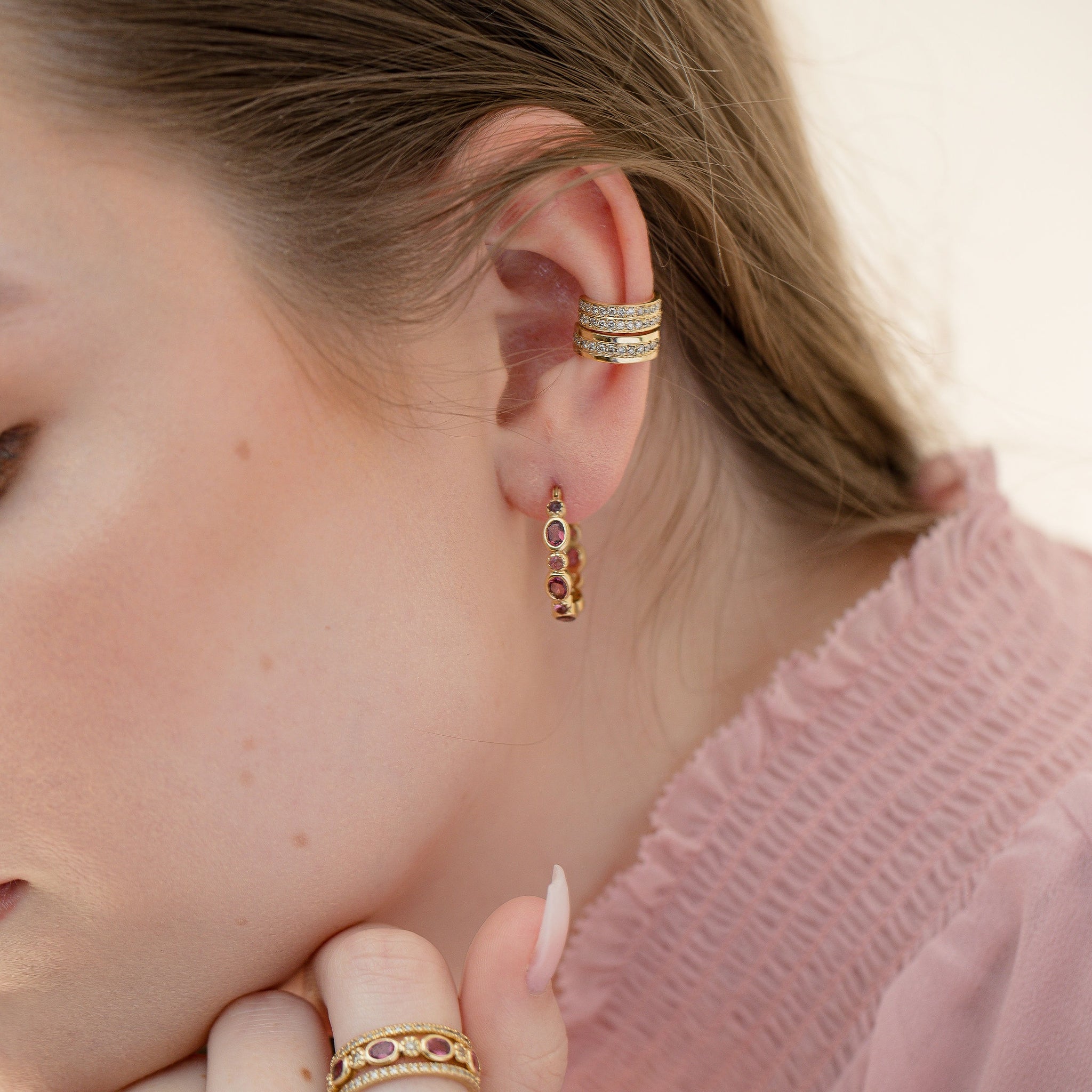 Close-up of a model wearing gold pink torumaline hoop earrings styled with diamonds huggies
