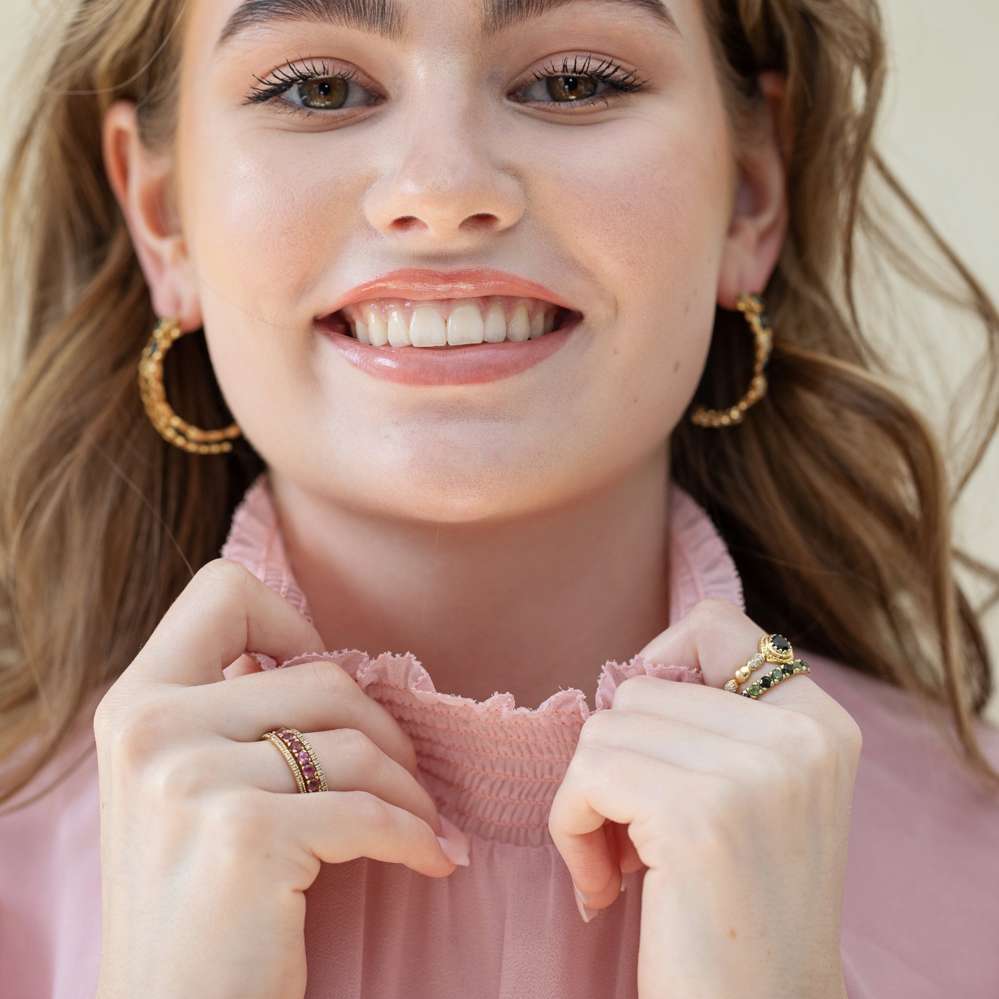 Front-facing view of a model wearing 18k gold earrings with green cabochon tourmalines and diamonds, styled with colorful stackable rings.