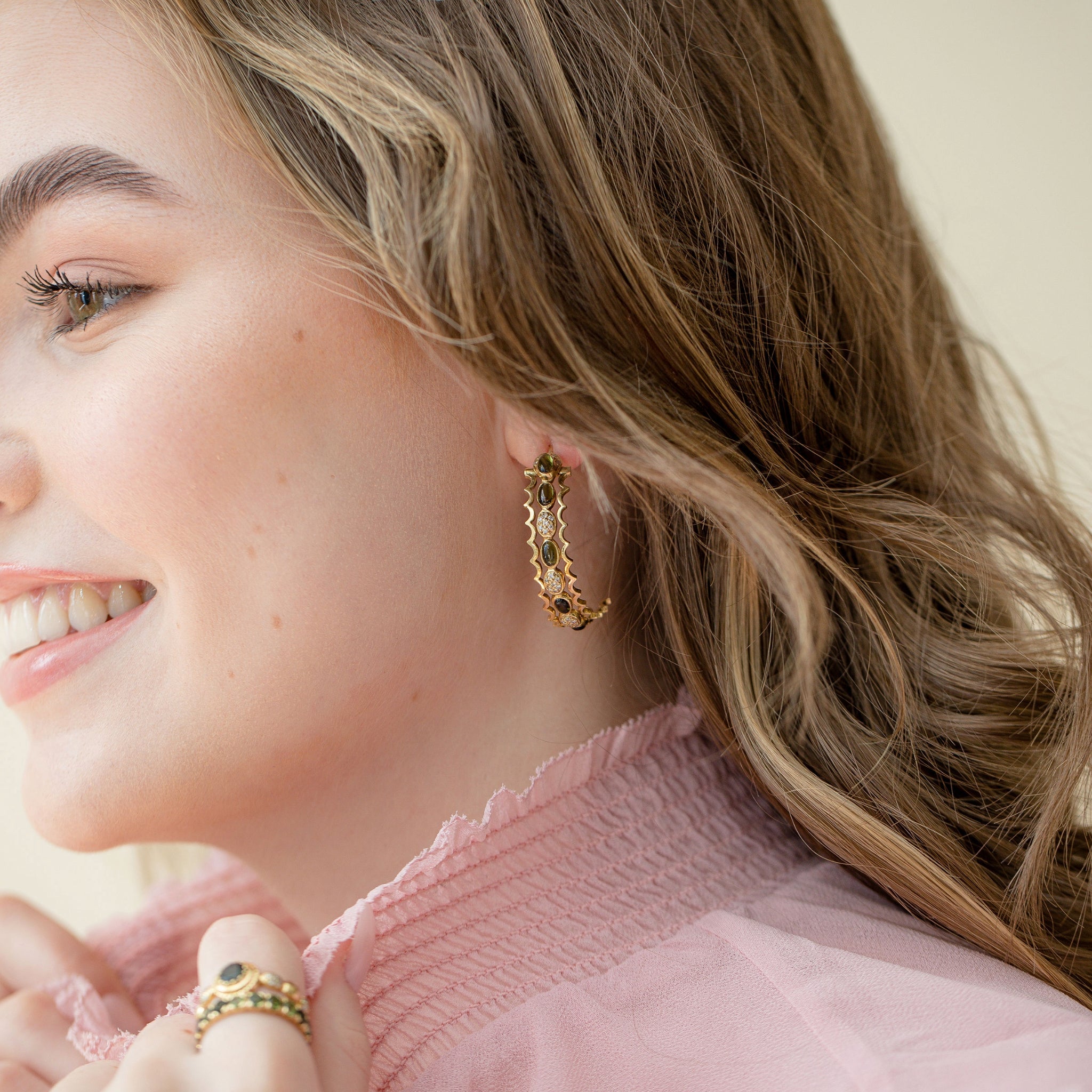 Close-up side view of a model wearing solid 18k gold hoop earrings featuring green cabochon tourmalines and diamonds.