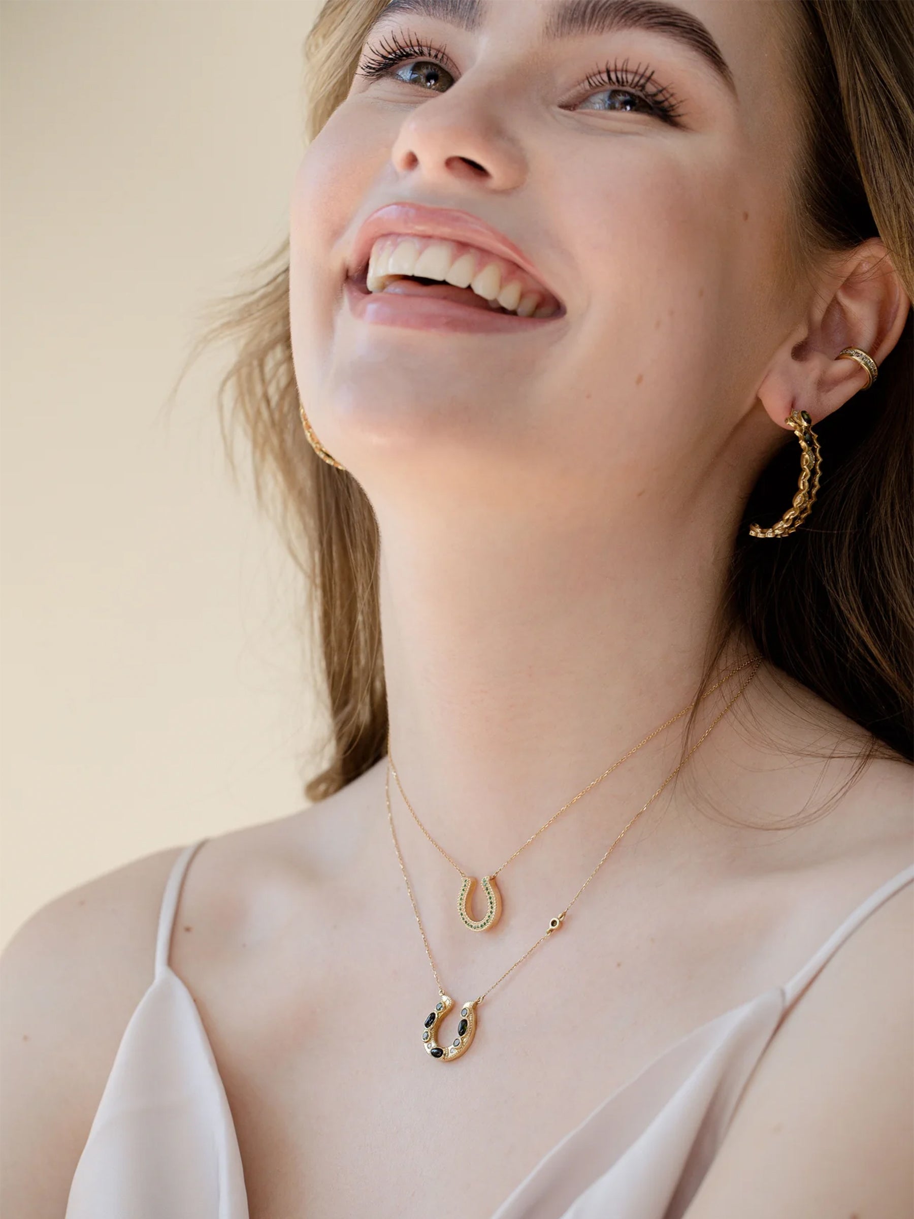 18k gold green tsavorite horseshoe necklace worn on model, minimal fine jewelry layered with another horseshoe necklace