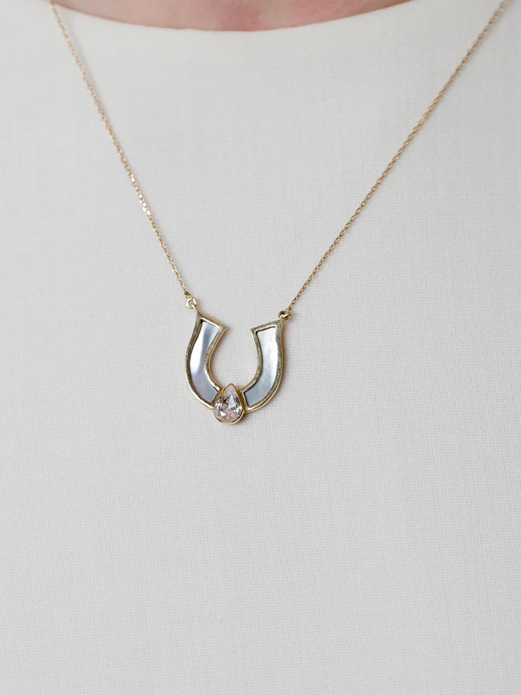 18k gold mother of pear horseshoe necklace with white sapphire, worn on model, minimal fine jewelry.