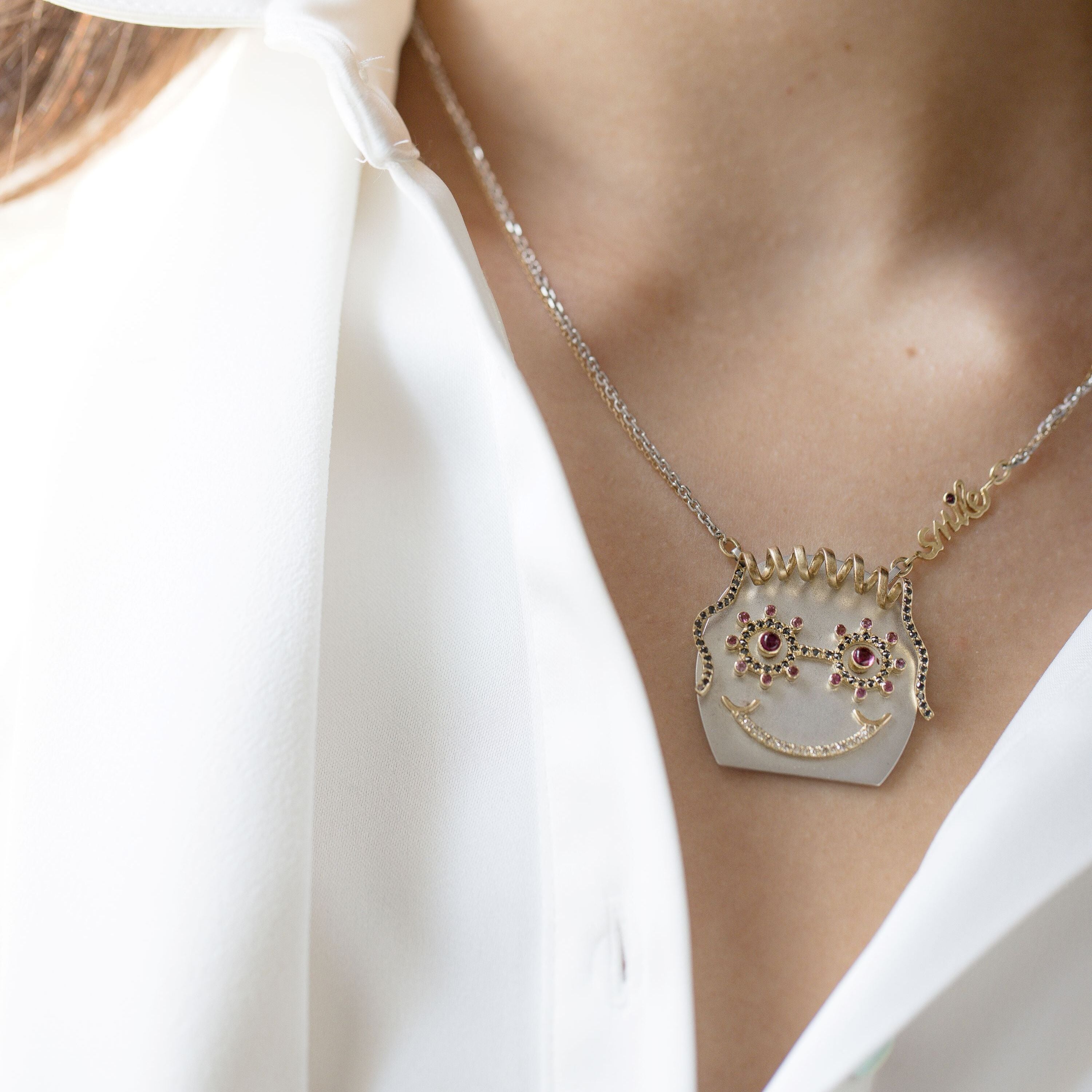 model wearing Gold & silver smiley face necklace, curly hair, black diamond glasses, diamond smile