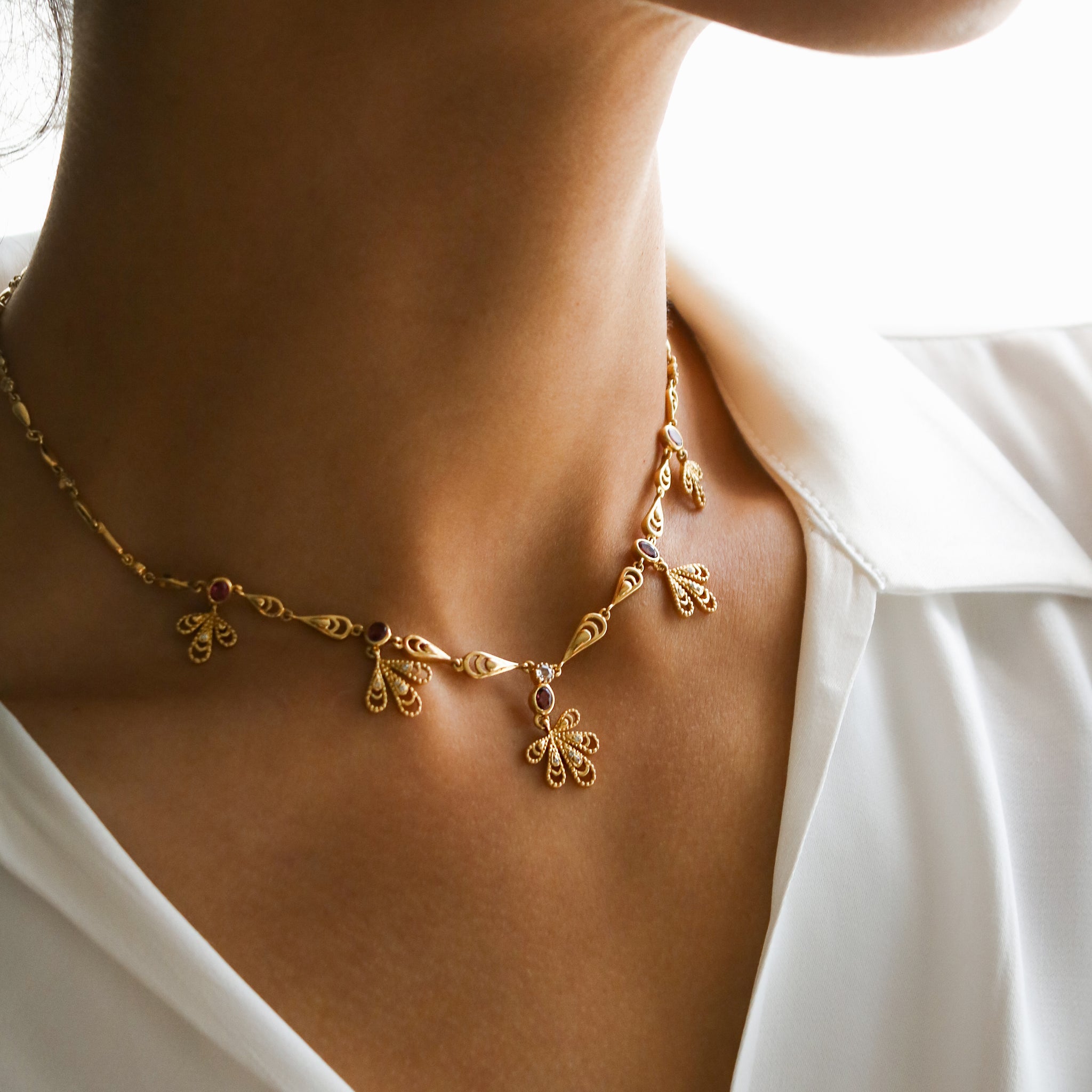 A model wearing the Aghabani Pergola Necklace by Hania Kuzbari, showcasing its gold design with pink tourmaline and diamonds as an elegant statement piece.