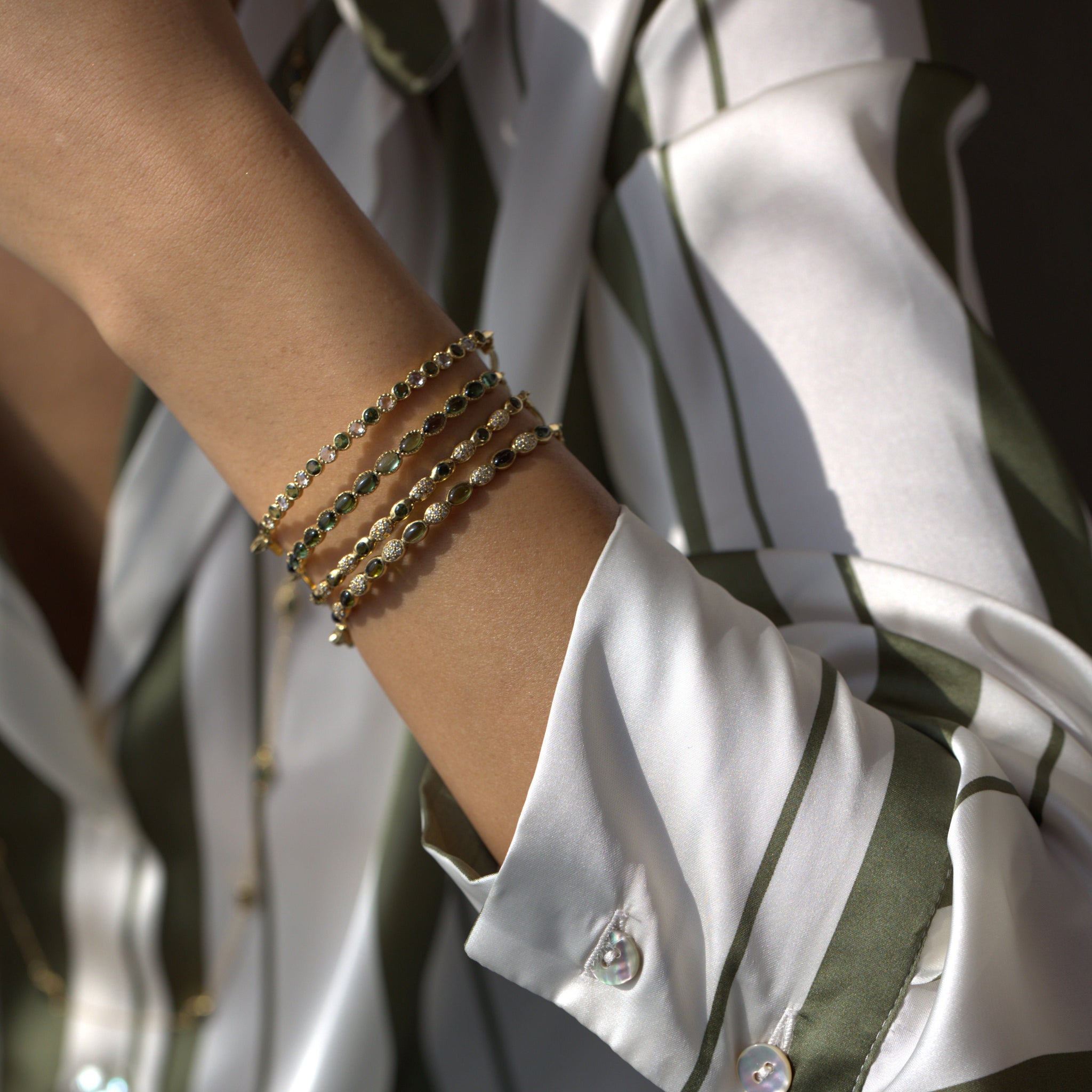 Model’s hand showcasing stacked gold bracelets with green tourmalines and diamonds.
