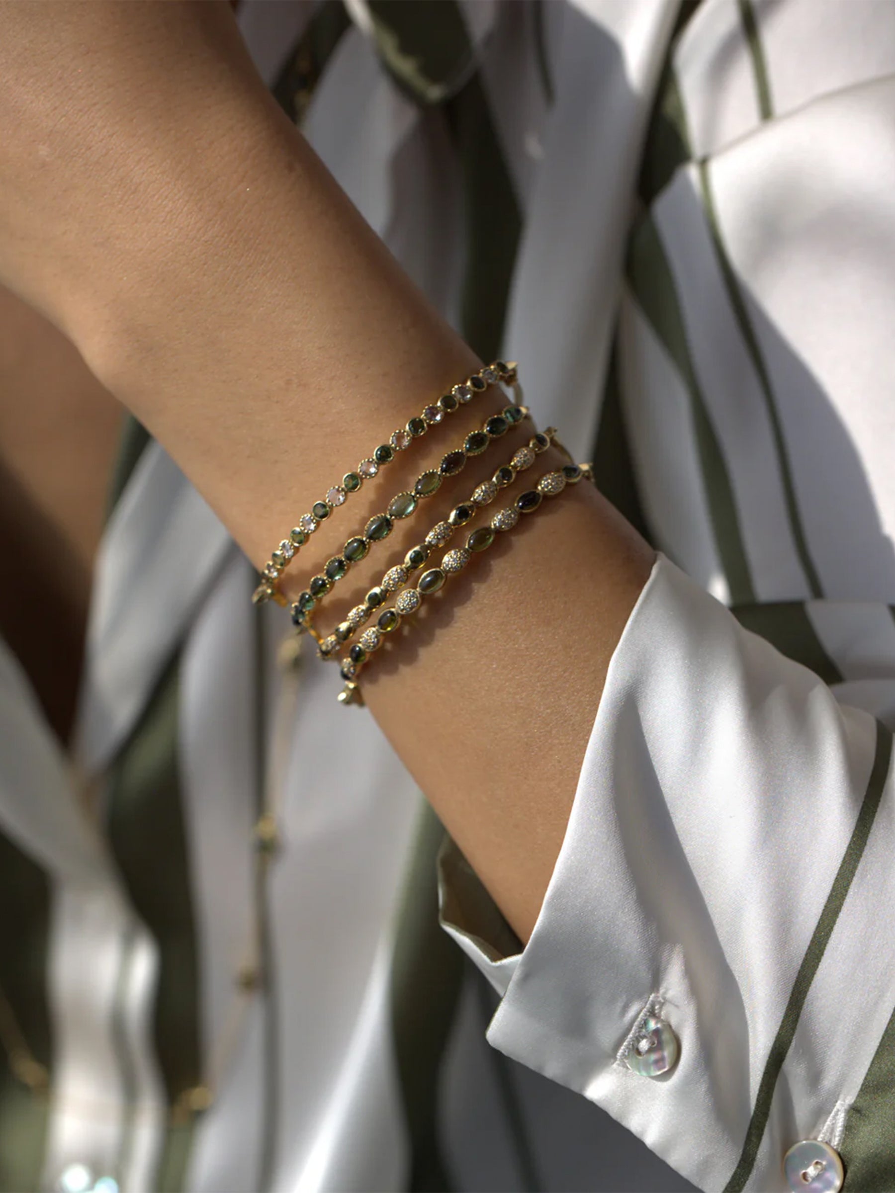 Close-up of a wrist wearing multiple gold freestyle green tourmaline bracelets. 