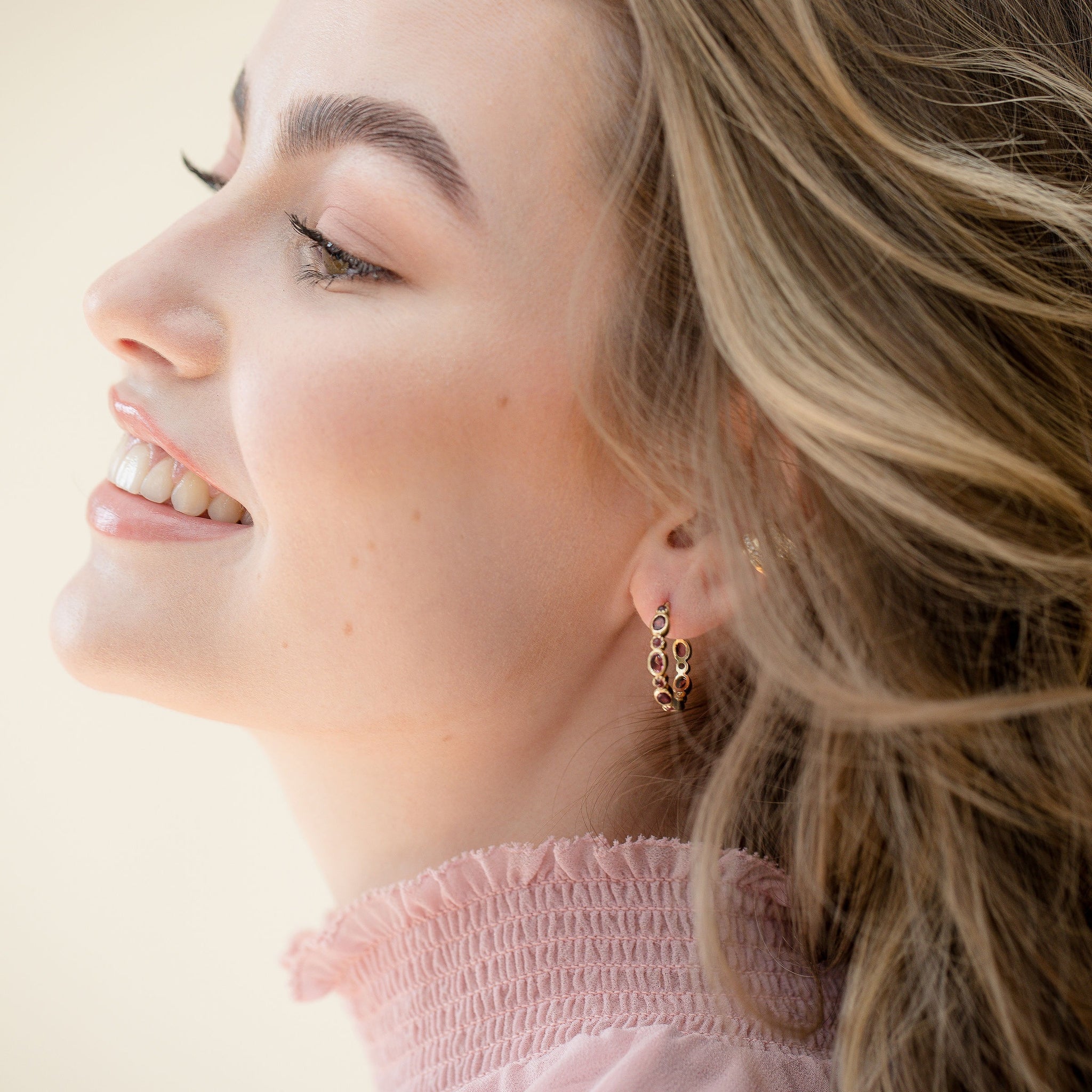 A close-up of a model wearing the gold pink tourmaline hoop earrings 