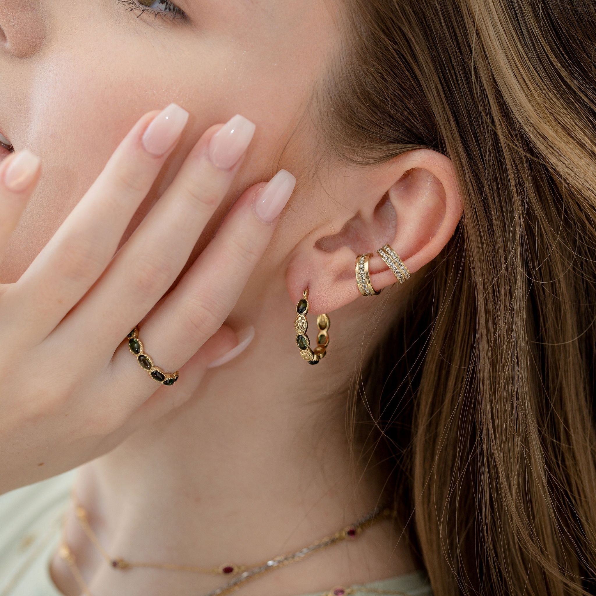 Model wearing Hania Kuzbari green tourmaline hoop earrings with stackable diamond huggies and a matching ring