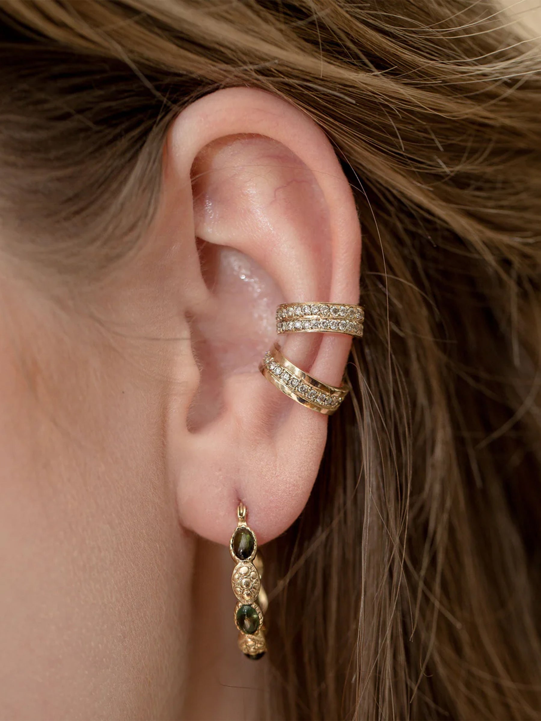 Close-up of an ear with gold hoop earrings and cuff earrings 