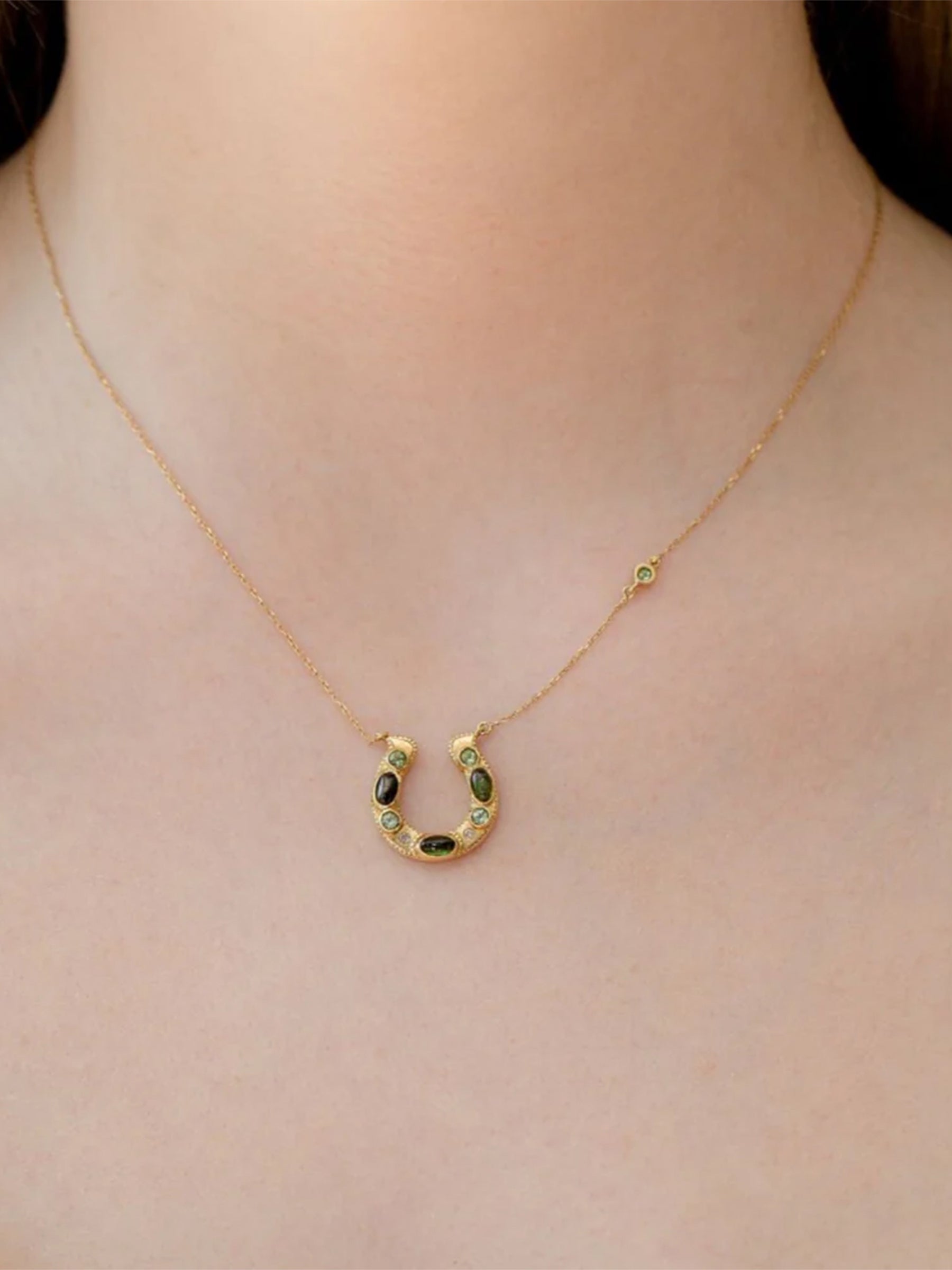 18k Gold Horseshoe Necklace with Green Tourmaline Cabochon and round Stones on model neck. 