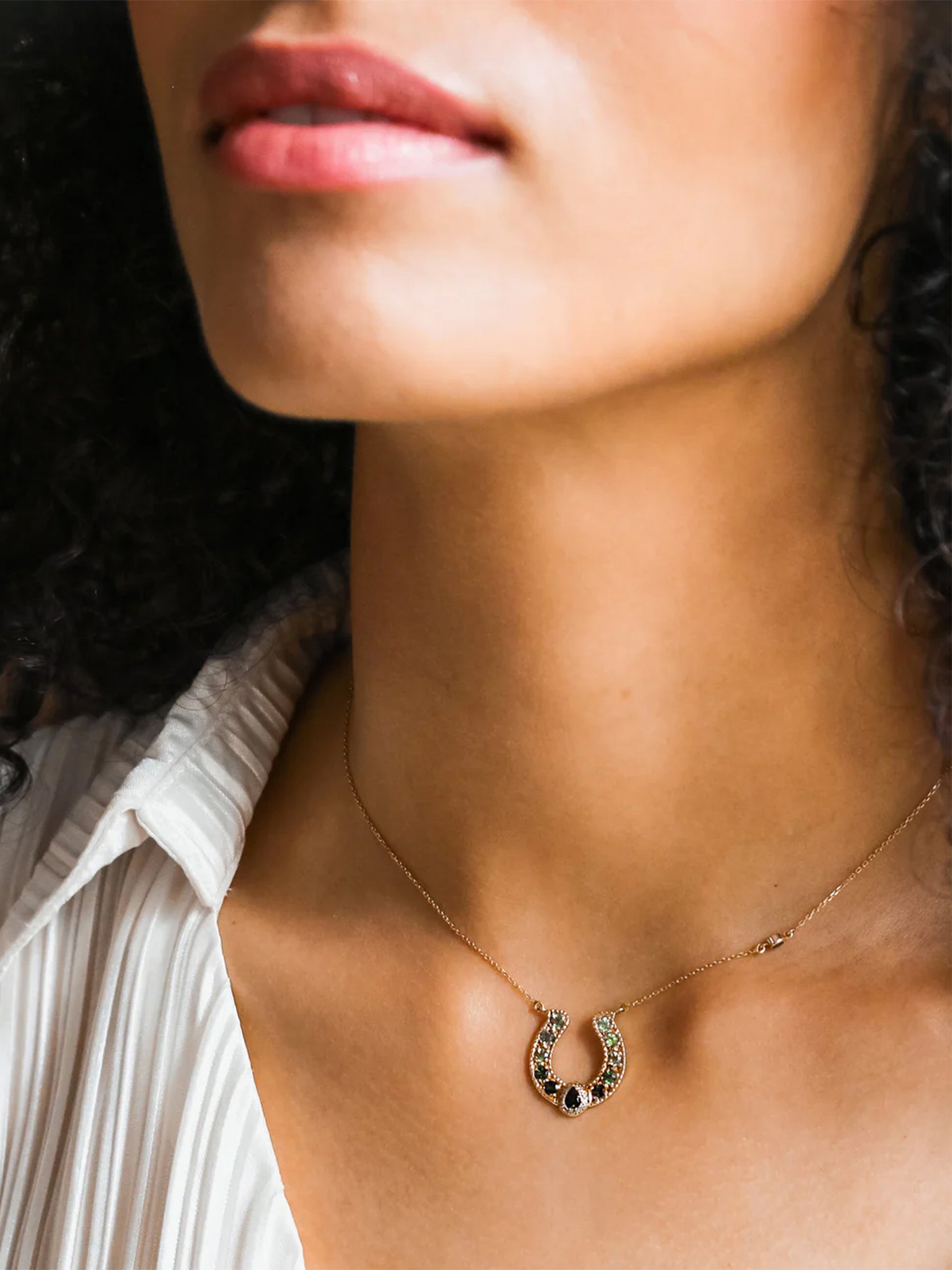 On-model front view of an 18k gold horseshoe pear crown green tourmaline necklace resting at the collarbone.