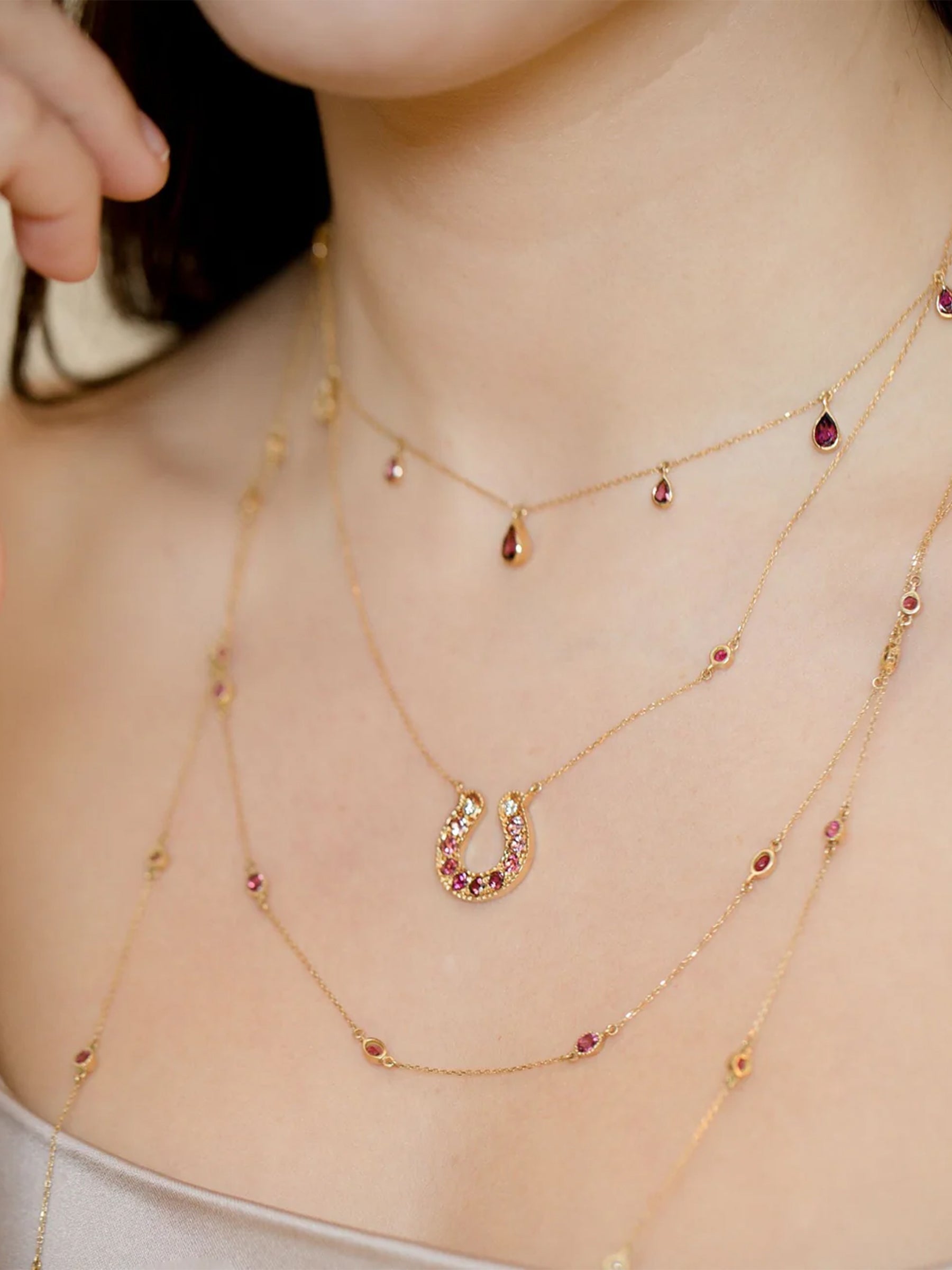 18k Gold Horseshoe Necklace with Green Tourmaline Ombré Gradient on a model layered with other pink tourmaline necklaces 