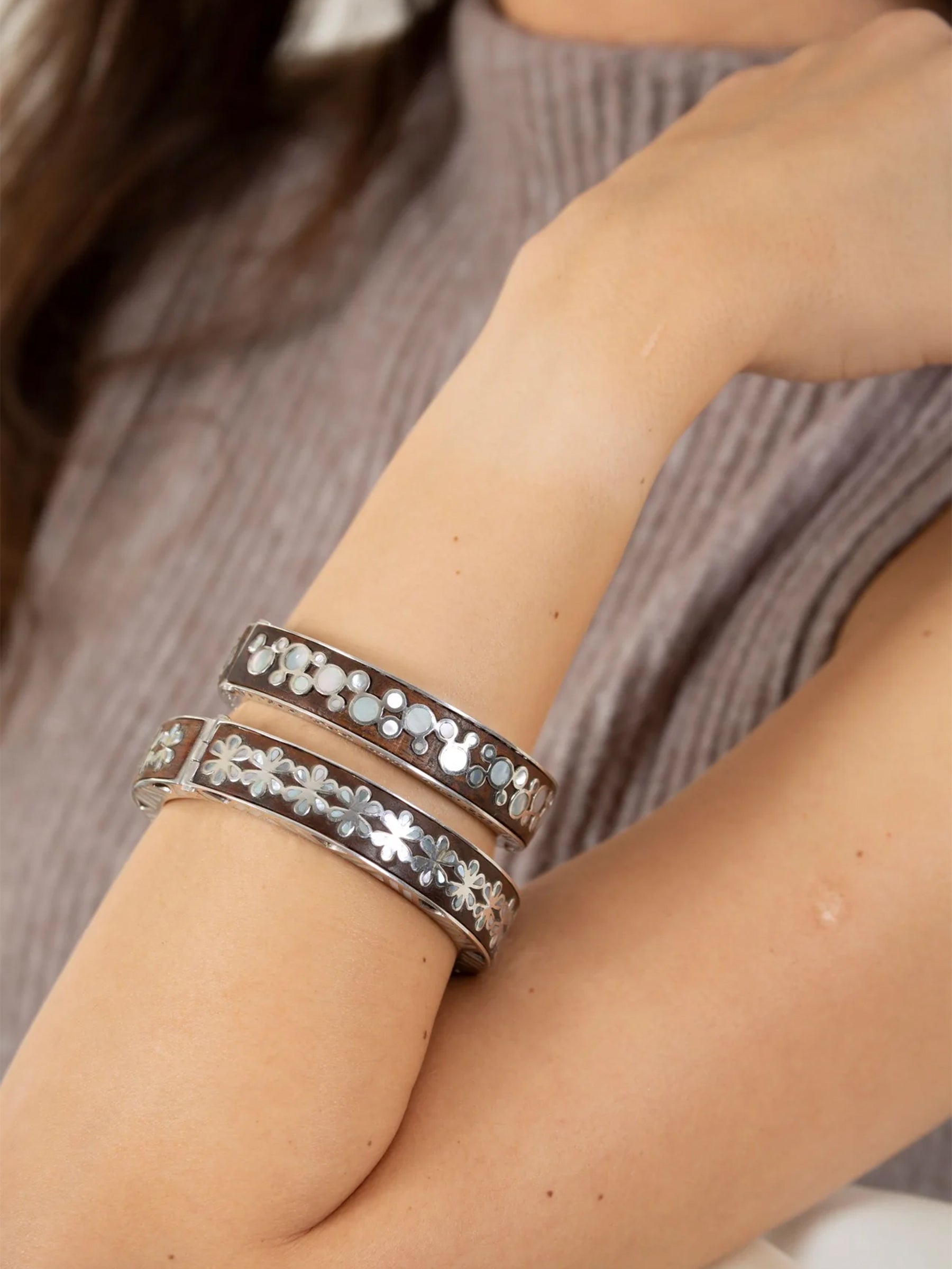 Close-up of a wrist wearing two silver bracelets inlayed with wood.