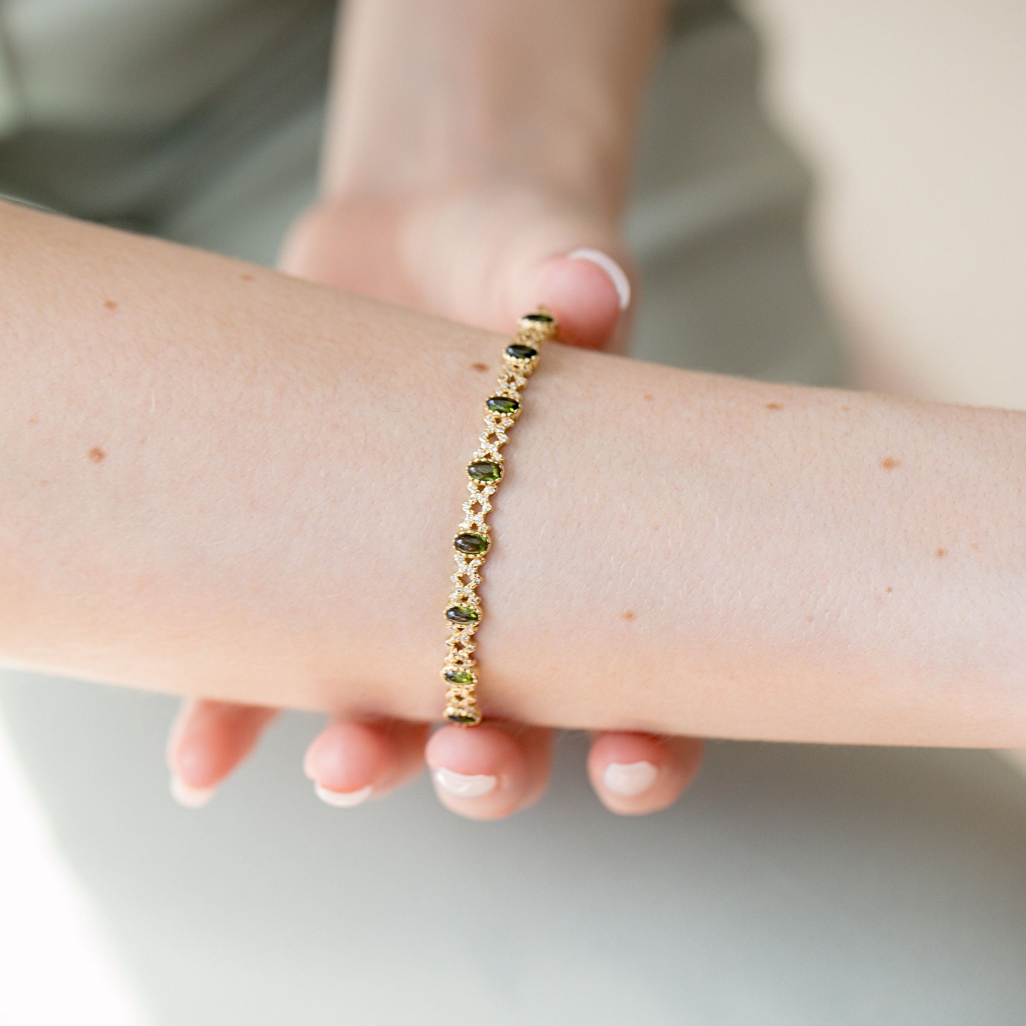 Close-up of model’s wrist wearing gold Freestyle Bracelet with green cabochon tourmalines and diamond rhombus details